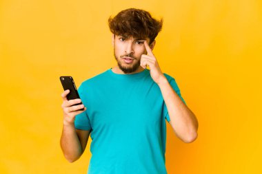 Genç Hintli bir adam işaret parmağıyla hayal kırıklığı gösteren bir telefon tutuyor..