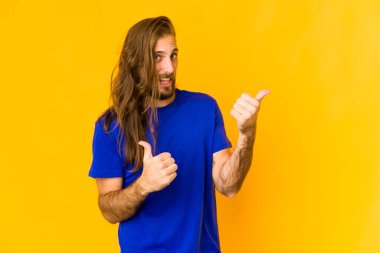 Uzun saçlı genç adam başparmağını kaldırıyor, gülümsüyor ve kendinden emin..