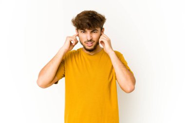 Beyaz arka plandaki genç Arap adam kulaklarını parmaklarıyla kapatıyor, gürültülü bir ortam yüzünden stresli ve çaresiz..