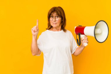 Orta yaşlı, beyaz bir kadın elinde bir numara olan bir megafonu parmağıyla tutuyor..