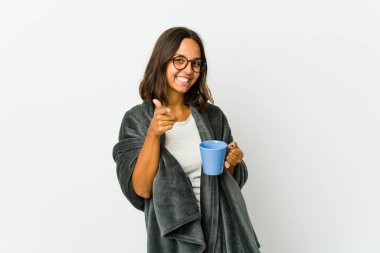 Beyaz arka planda battaniyeli genç Latin kadın. Önü işaret eden neşeli gülümsemeler..