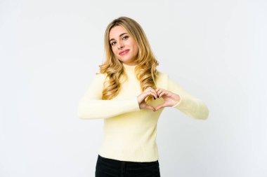 Beyaz tenli sarışın kadın gülümsüyor ve elleriyle kalp şeklini gösteriyor..