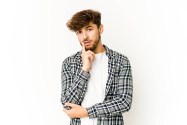 Beyaz arka planda genç bir Arap şüpheli ve şüpheci bir ifadeyle yana bakıyor..