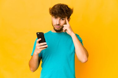 Elinde bir telefon tutan genç Hintli bir adam şakağı parmağıyla işaret ediyor, düşünüyor ve bir göreve odaklanıyor..