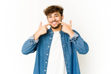 Beyaz arka plandaki genç Arap adam gülümsüyor, parmaklarını ağıza doğrultuyor..