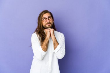 Uzun saçlı genç adam ellerini çenesinin altında tutuyor, mutlu bir şekilde yan tarafa bakıyor..