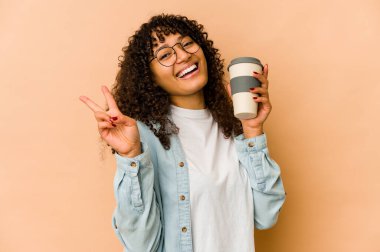 Afro-Amerikan Afro kadın elinde kahveyle neşeli ve tasasız bir şekilde barış sembolü taşıyor..