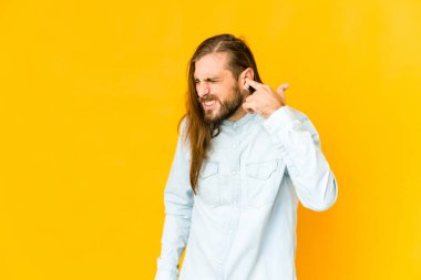 Uzun saçlı genç adam elleriyle kulaklarını kapatıyor..