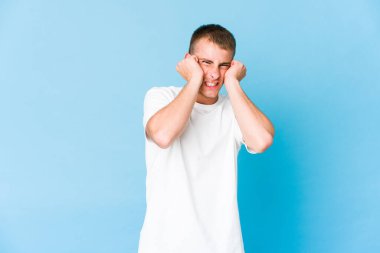 Genç, beyaz, yakışıklı adam kulaklarını elleriyle kapatıyor..