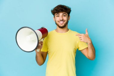 Genç bir Arap, elinde megafoncuyla gömlek fotokopi odasını işaret ediyor, gururlu ve kendinden emin