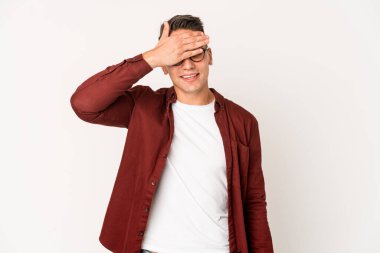 Genç, beyaz tenli yakışıklı, izole edilmiş, elleriyle gözlerini kapatmış, gülümseyerek bir sürpriz bekliyor..