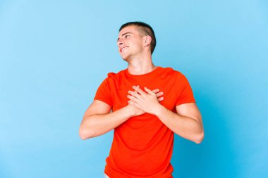 Genç, beyaz, yakışıklı bir adam gülüyor. Elini yüreğine koyuyor. Mutluluk kavramı..