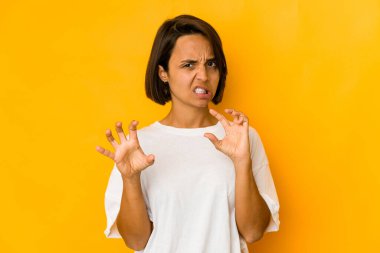 Sarı renkte izole edilmiş genç İspanyol kadın pençelerini kedi taklidi yaparken gösteriyor, agresif bir hareket..