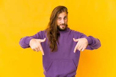 Uzun saçlı genç adam parmaklarıyla işaret ediyor, olumlu bir his..