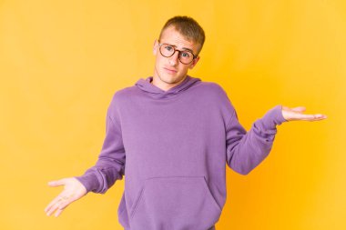 Kafası karışmış, genç, beyaz, yakışıklı bir adam. Kopyasını tutmak için omuz silkiyor..