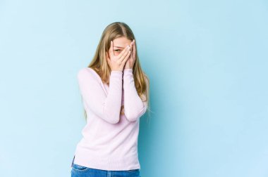 Mavi arka planda izole edilmiş genç sarışın kadın, korkmuş ve gergin parmaklarıyla göz kırp..