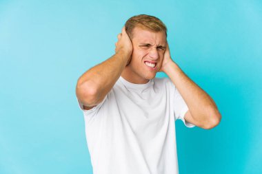 Genç, beyaz, yakışıklı adam kulaklarını elleriyle kapatıyor..