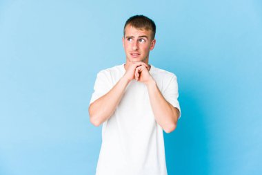 Beyaz tenli yakışıklı adam ellerini çenesinin altında tutuyor ve mutlu bir şekilde yan tarafa bakıyor..