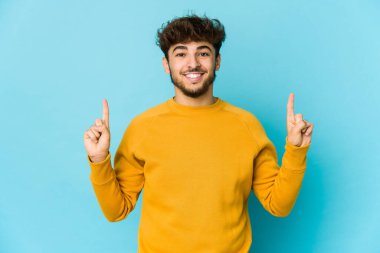 Mavi arka plandaki genç Arap, iki ön parmağı da boş bir alan gösterirken....