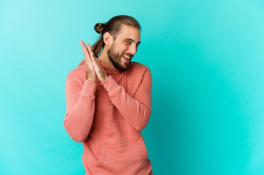 Uzun saçlı genç adam enerjik ve rahat görünüyor, ellerini ovuşturarak kendinden emin..