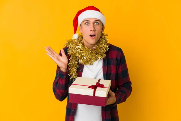 Junge Kaukasische Mann Mit Weihnachtsmütze Hält Ein Geschenk Isoliert Auf — Stockfoto