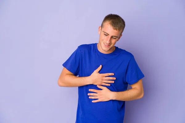 Young caucasian handsome man laughs happily and has fun keeping hands on stomach.