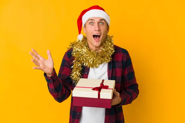 头戴圣诞礼帽 头戴黄色背景的年轻的高加索人 收到了一个令人愉快的惊喜 兴奋和举手的礼物 — 图库照片