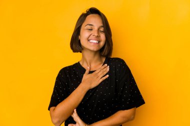Sarı üzerine izole edilmiş genç İspanyol kadın yüksek sesle gülüyor elini göğsüne koyuyor.