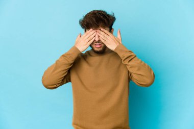 Mavi arka plandaki genç Arap adam elleriyle gözlerini kapatmaktan korkuyor..