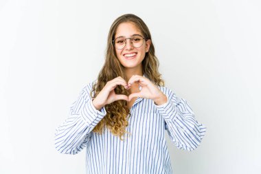 Genç beyaz kadın gülümsüyor ve elleriyle kalp şeklini gösteriyor..