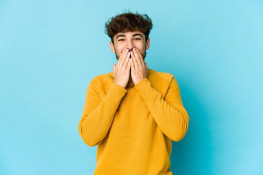 Mavi arka planda genç bir Arap bir şeye gülüyor, elleriyle ağzını kapatıyor..