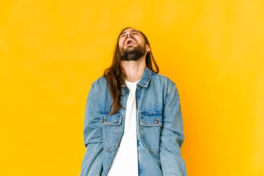 Uzun saçlı genç adam rahat görünüyor ve mutlu gülüyor, boynunu uzatmış dişlerini gösteriyor..