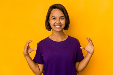 Genç İspanyol kadın sarıda izole edilmiş. Elinde avuç içi olan bir şeyle kameraya sunuyor..