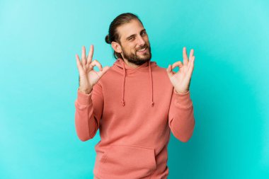 Uzun saçlı genç adam neşeli ve kendinden emin görünüyor..