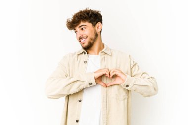 Beyaz arka plandaki genç Arap adam gülümsüyor ve elleriyle kalp şeklini gösteriyor..