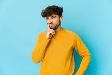 Mavi arka planda genç bir Arap adam bir strateji planlıyor, bir iş yolu düşünüyor..