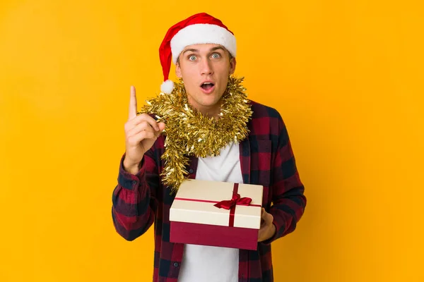 クリスマスの帽子をかぶった若い白人男性は アイデア インスピレーションの概念を持っている黄色の背景に孤立した存在を保持しています — ストック写真