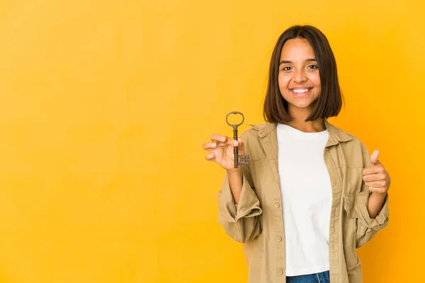 Young hispanic woman holding an old key smiling and raising thumb up