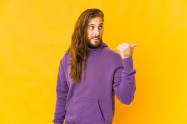 Uzun saçlı genç adam başparmağıyla işaret ediyor, gülüyor ve kaygısız..