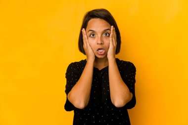 Genç İspanyol kadın sarıda izole edilmiş. Yüzünün yarısını avuç içiyle kaplayarak eğleniyor..