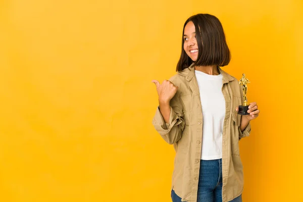 Young Hispanic Woman Holding Award Statuette Points Thumb Finger Away — Stockfoto