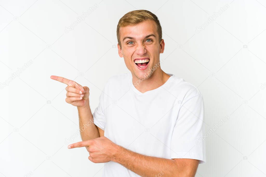 Young caucasian handsome man pointing with forefingers to a copy space, expressing excitement and desire.