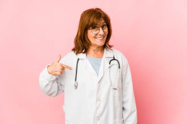 Middle age caucasian doctor woman isolated person pointing by hand to a shirt copy space, proud and confident