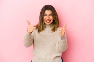 Pembe arka planda izole edilmiş genç Hintli kadın gülümsüyor ve başparmağını kaldırıyor.