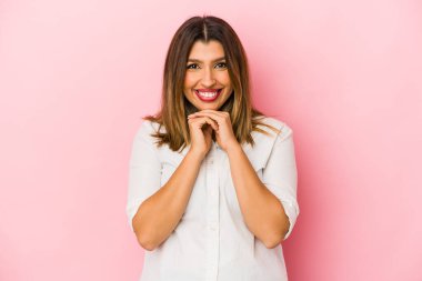 Pembe arka planda izole edilmiş genç Hintli kadın ellerini çenesinin altında tutuyor, mutlu bir şekilde yana bakıyor..