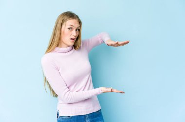 Mavi arka planda izole edilmiş genç sarışın kadın elleri arasında bir kopya alanı tutarken şok olmuş ve hayrete düşmüştü..