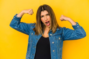 Sarı arka planda izole edilmiş genç bir Hintli kadın güçlü bir hareket sergiliyor. Kadınsı gücün sembolü.