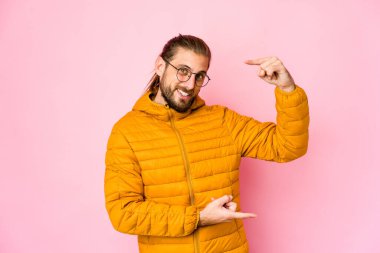 Uzun saçlı genç adam işaret parmaklarıyla küçük bir şey tutuyor, gülümsüyor ve kendinden emin..