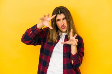 Sarı arka planda izole edilmiş genç Hintli kadın pençelerini kedi taklidi yaparken gösteriyor, agresif bir hareket..