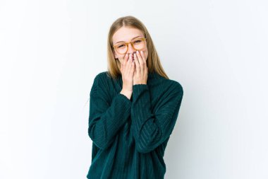 Beyaz arka planda izole edilmiş genç sarışın bir kadın bir şeye gülüyor, elleriyle ağzını kapatıyor..